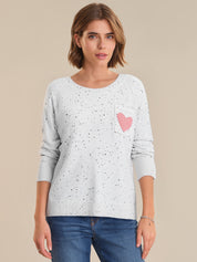 Woman wearing a light gray sweater with a pink heart design on a beige background
