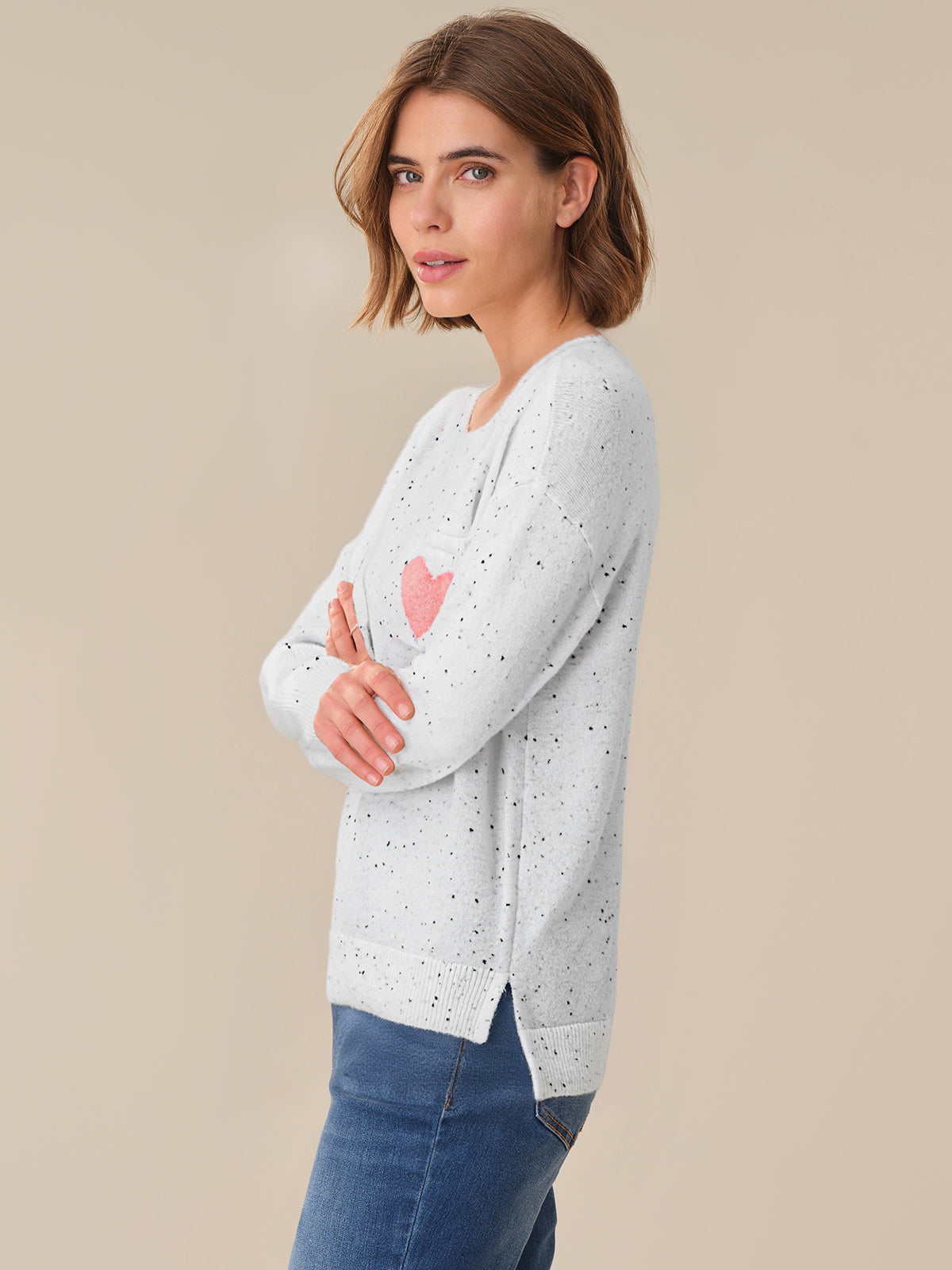 Woman wearing a light gray sweater with a pink heart design on a beige background