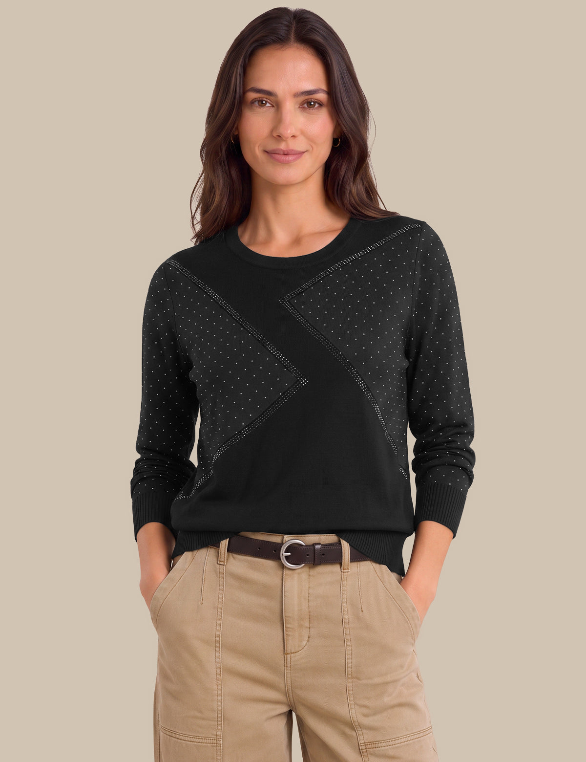A woman modeling a black long-sleeve knit sweater with textured geometric panel details on the chest, paired with beige cargo pants, against a solid beige background.