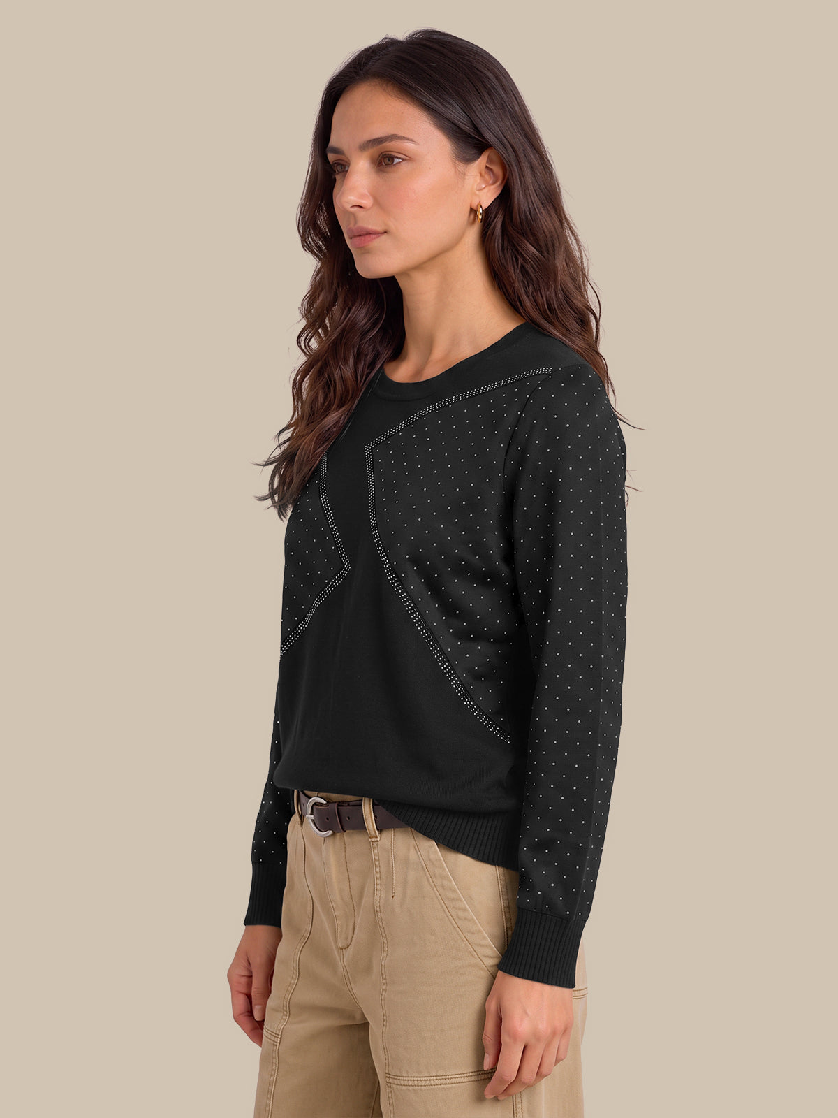 A woman wearing a black long-sleeve knit sweater with subtle dotted texture details and beige cargo pants, photographed against a solid beige studio background.