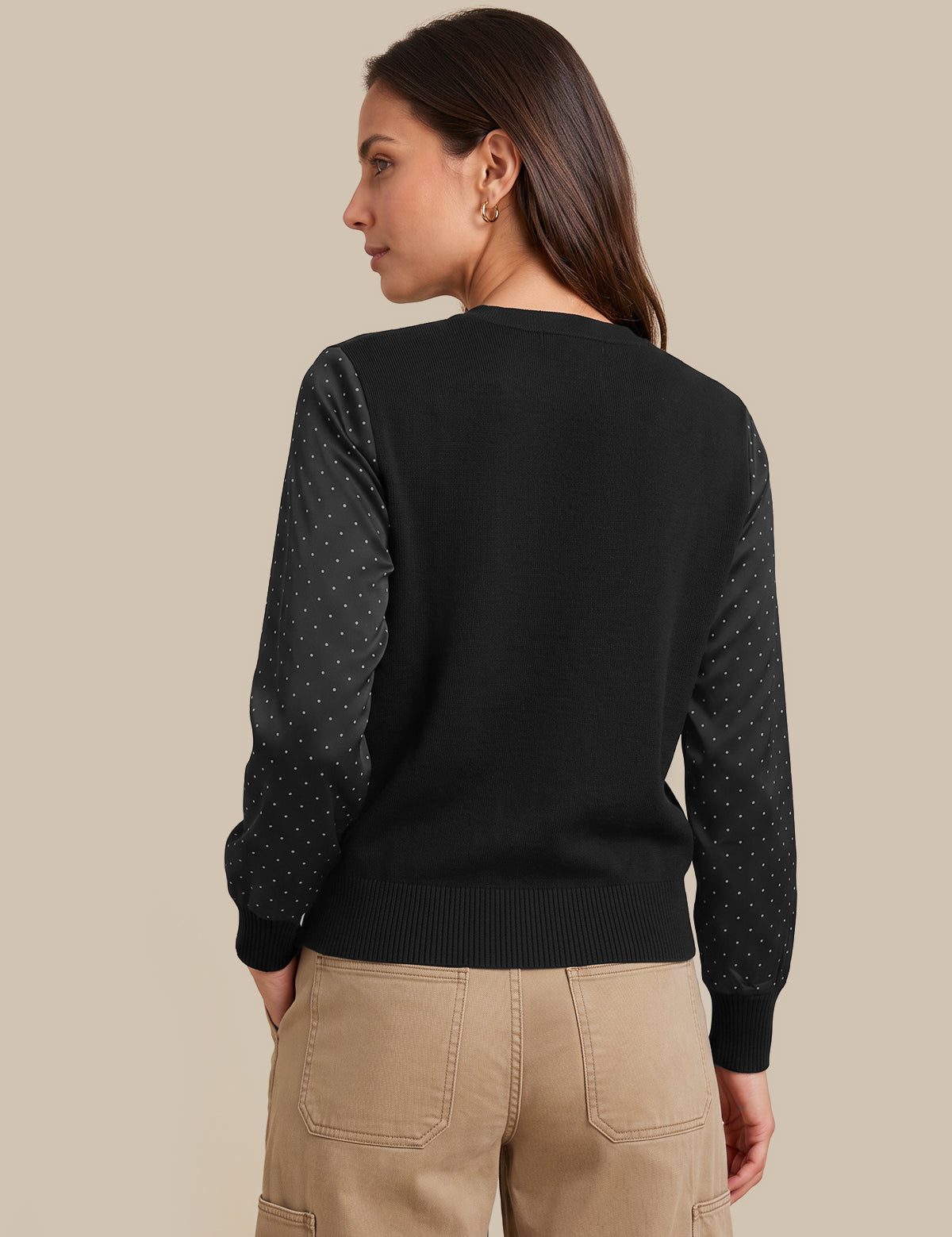 A woman shown from the back wearing a black knit sweater with sheer dotted sleeves and tan cargo pants, against a plain beige studio background.
