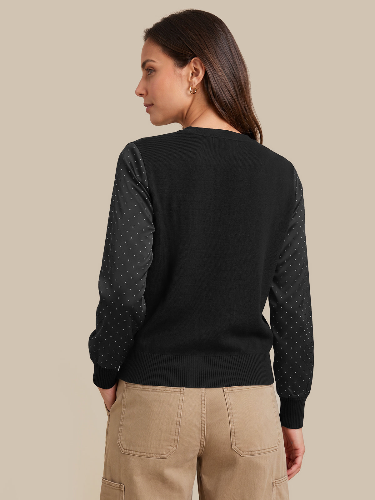 A woman shown from the back wearing a black knit sweater with sheer dotted sleeves and tan cargo pants, against a plain beige studio background.