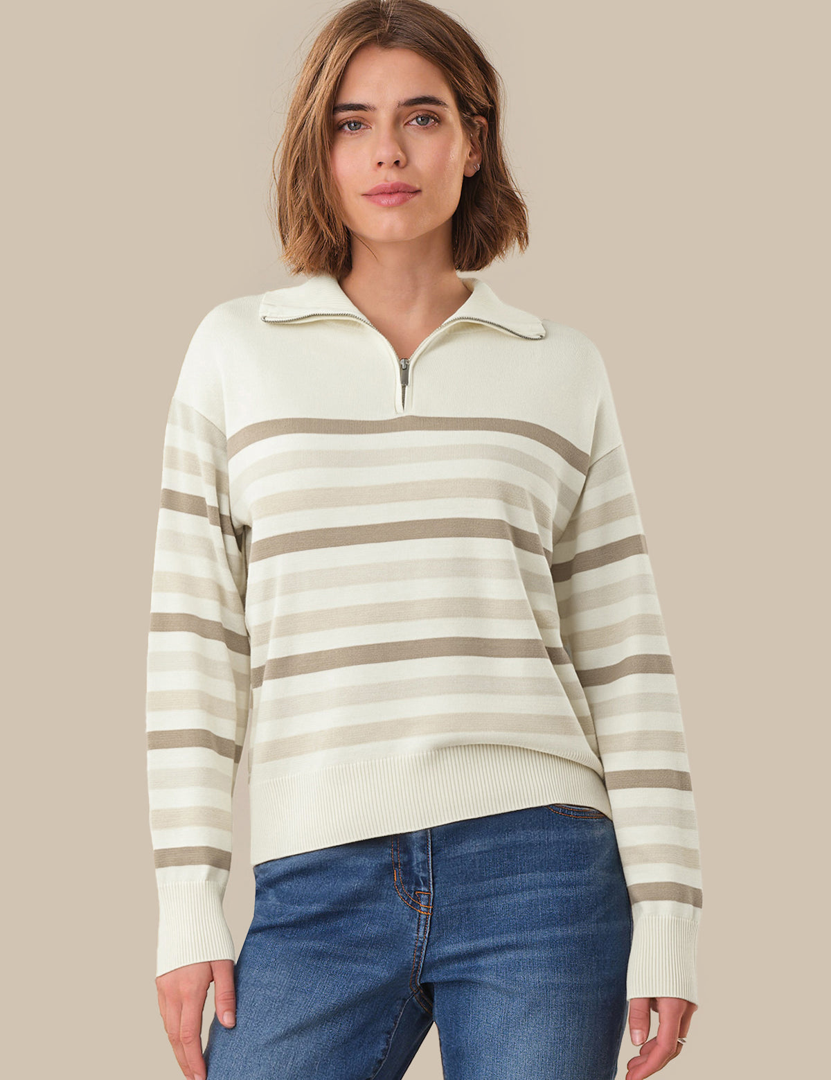 Woman wearing a striped sweater and blue jeans against a beige background
