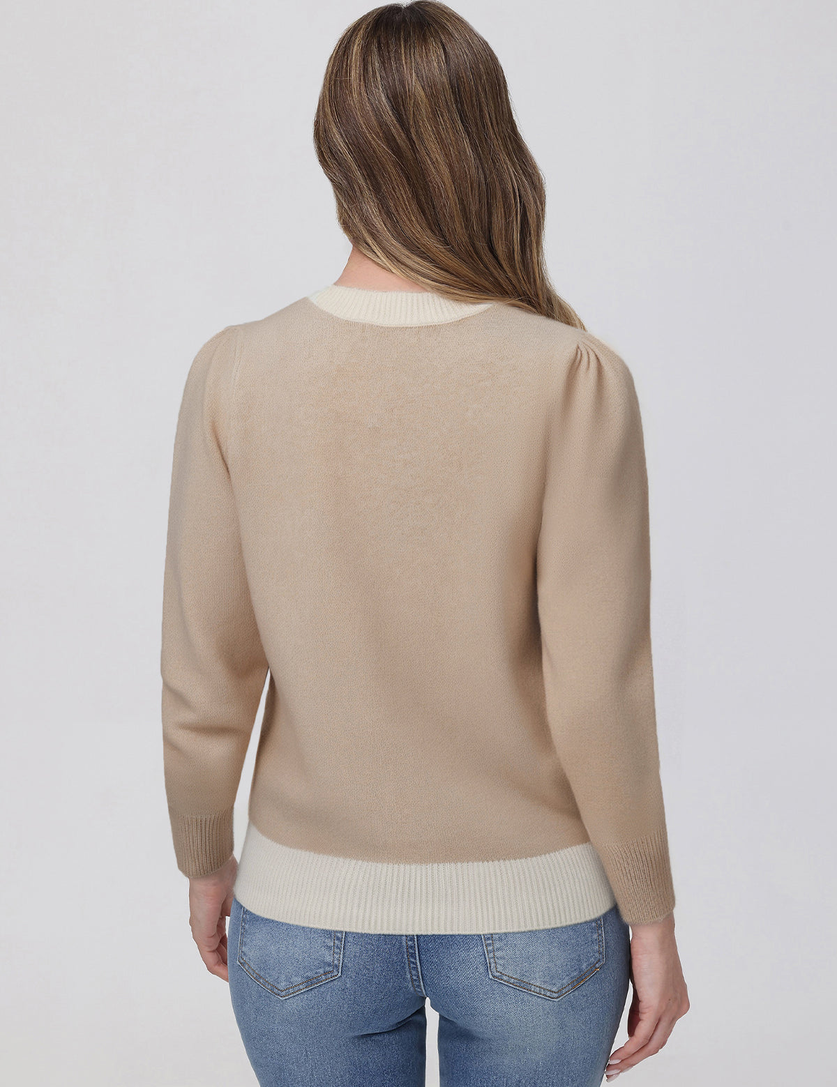 Woman wearing a beige sweater and blue jeans on a white background