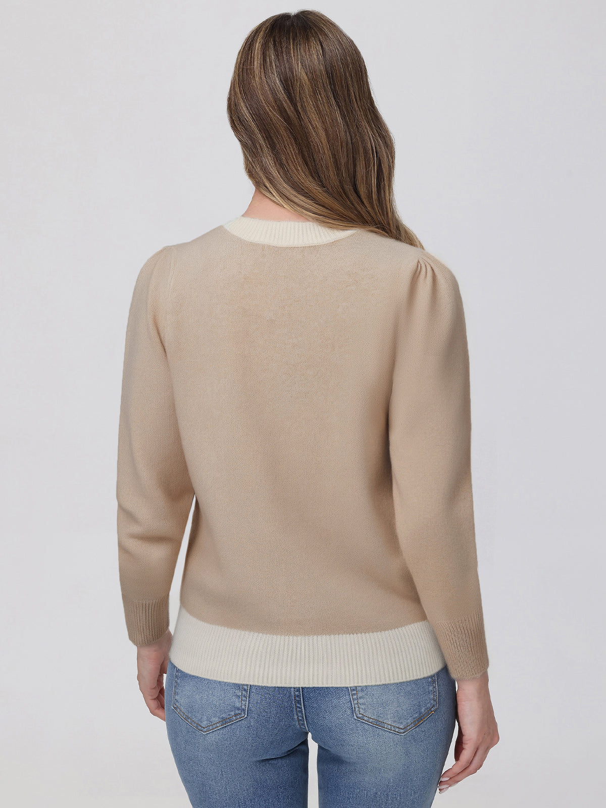 Woman wearing a beige sweater and blue jeans on a white background