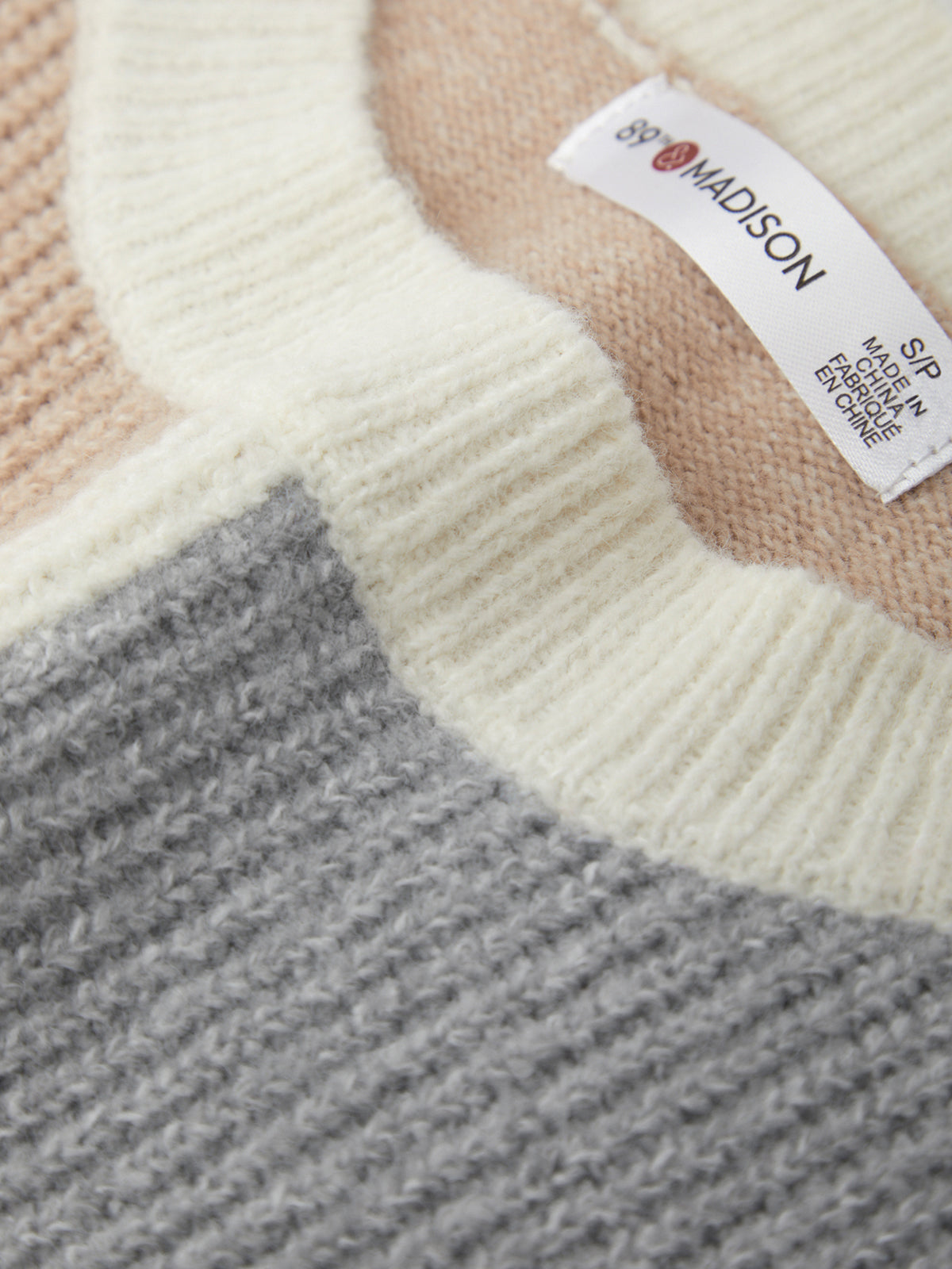 Close-up of a knit fabric with a label on a sweater, featuring shades of beige, gray, and white.