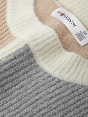 Close-up of a knit fabric with a label on a sweater, featuring shades of beige, gray, and white.