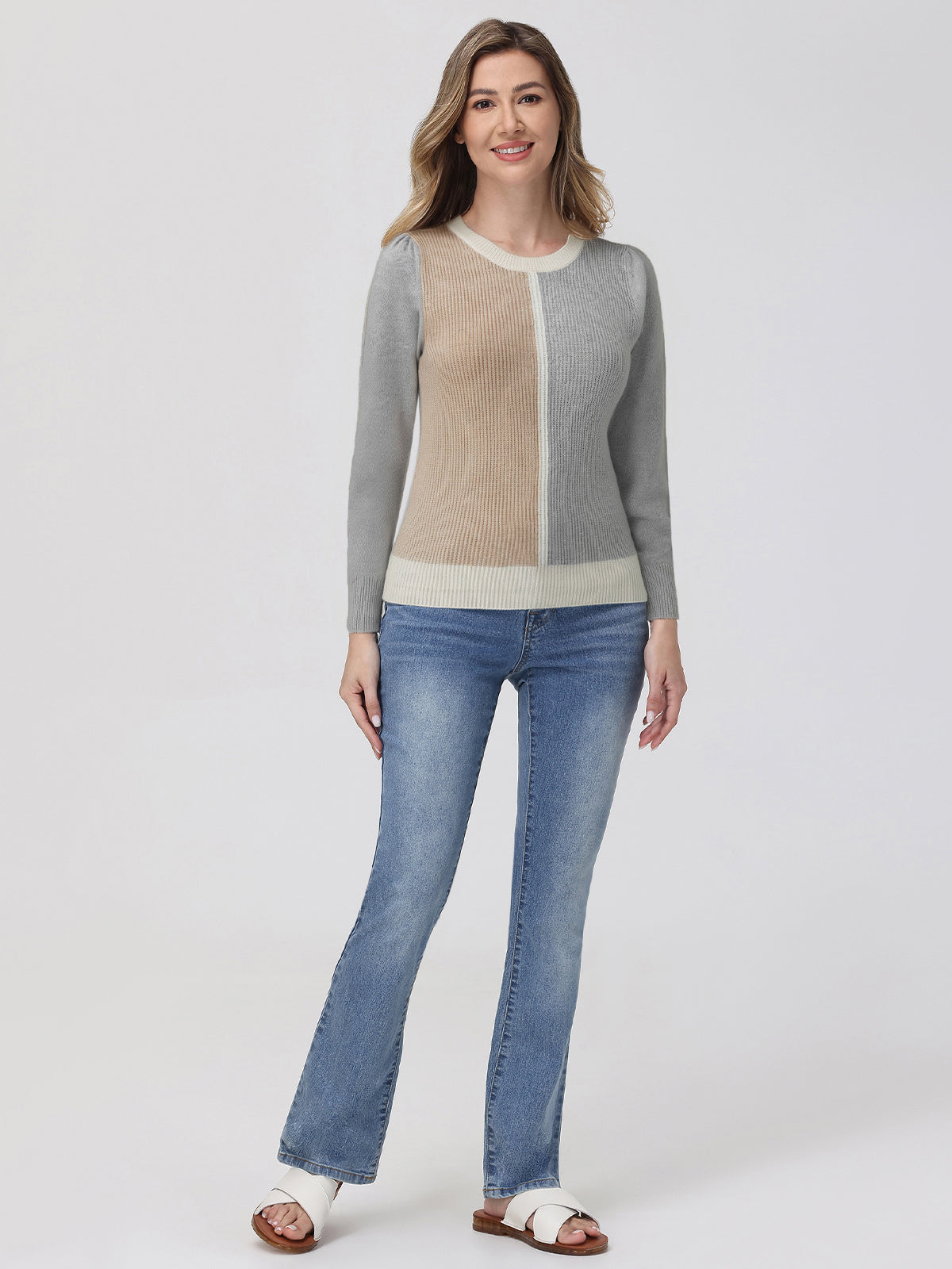 Woman wearing a gray and beige sweater with blue jeans on a white background
