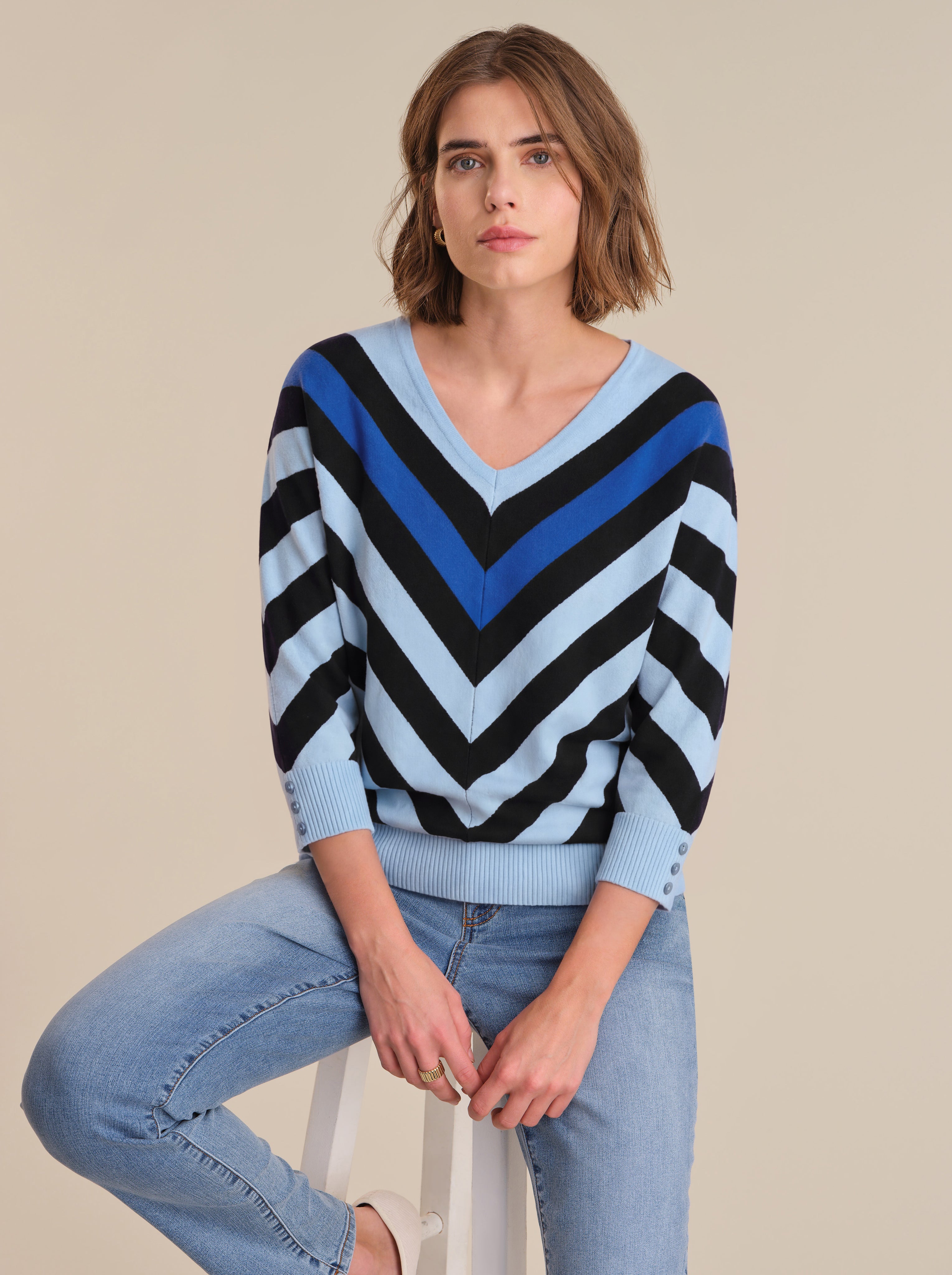 Woman wearing a blue and black striped sweater with light blue jeans on a beige background