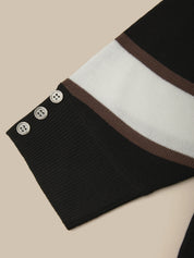 Close-up of a ribbed knit sweater sleeve in black, white, and brown stripes, featuring three decorative buttons on the cuff, set against a solid beige background.