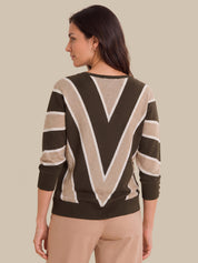A woman shown from the back wearing a knit sweater with a bold geometric pattern in dark brown, beige, and white, paired with beige trousers, against a solid beige background.