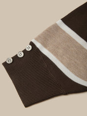 Close-up of a ribbed knit sweater sleeve cuff in dark brown, featuring a beige and white striped section and three decorative buttons.