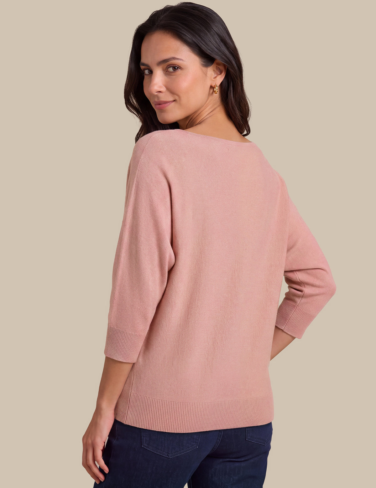A woman wearing a dusty pink knit sweater with three-quarter sleeves, shown from a three-quarter back angle against a solid beige background.