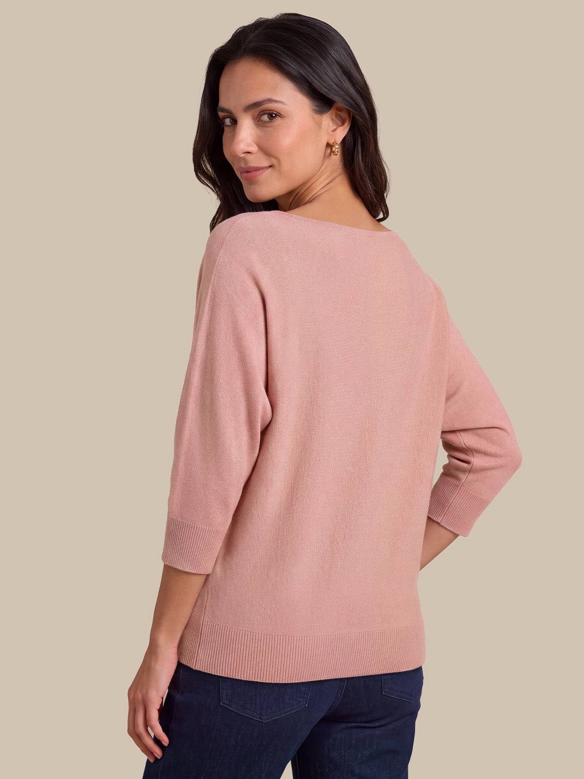 A woman wearing a dusty pink knit sweater with three-quarter sleeves, shown from a three-quarter back angle against a solid beige background.