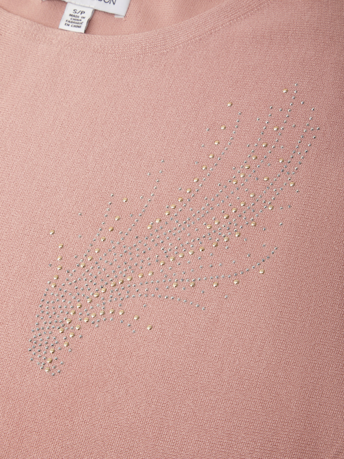 Close-up of a dusty pink knit top with a rhinestone embellishment forming a stylized feather or wing shape on the chest.
