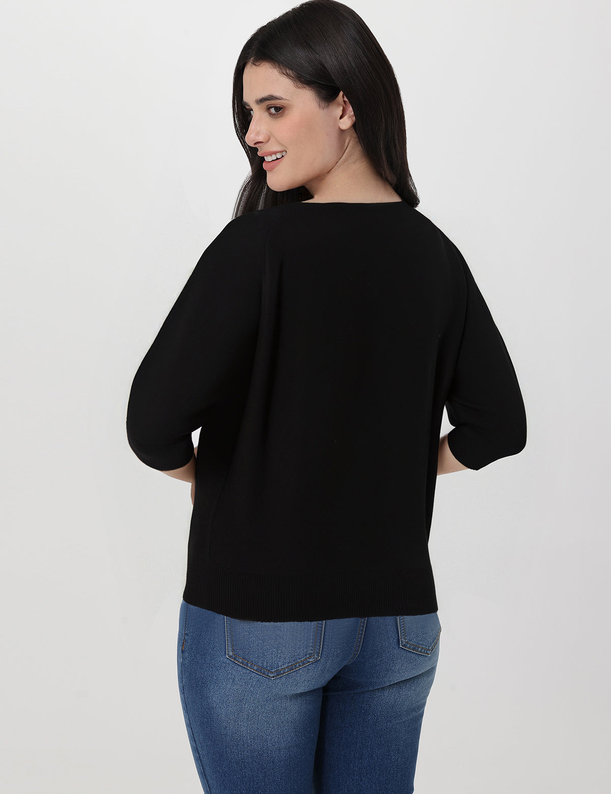 Woman wearing a black sweater and blue jeans on a white background