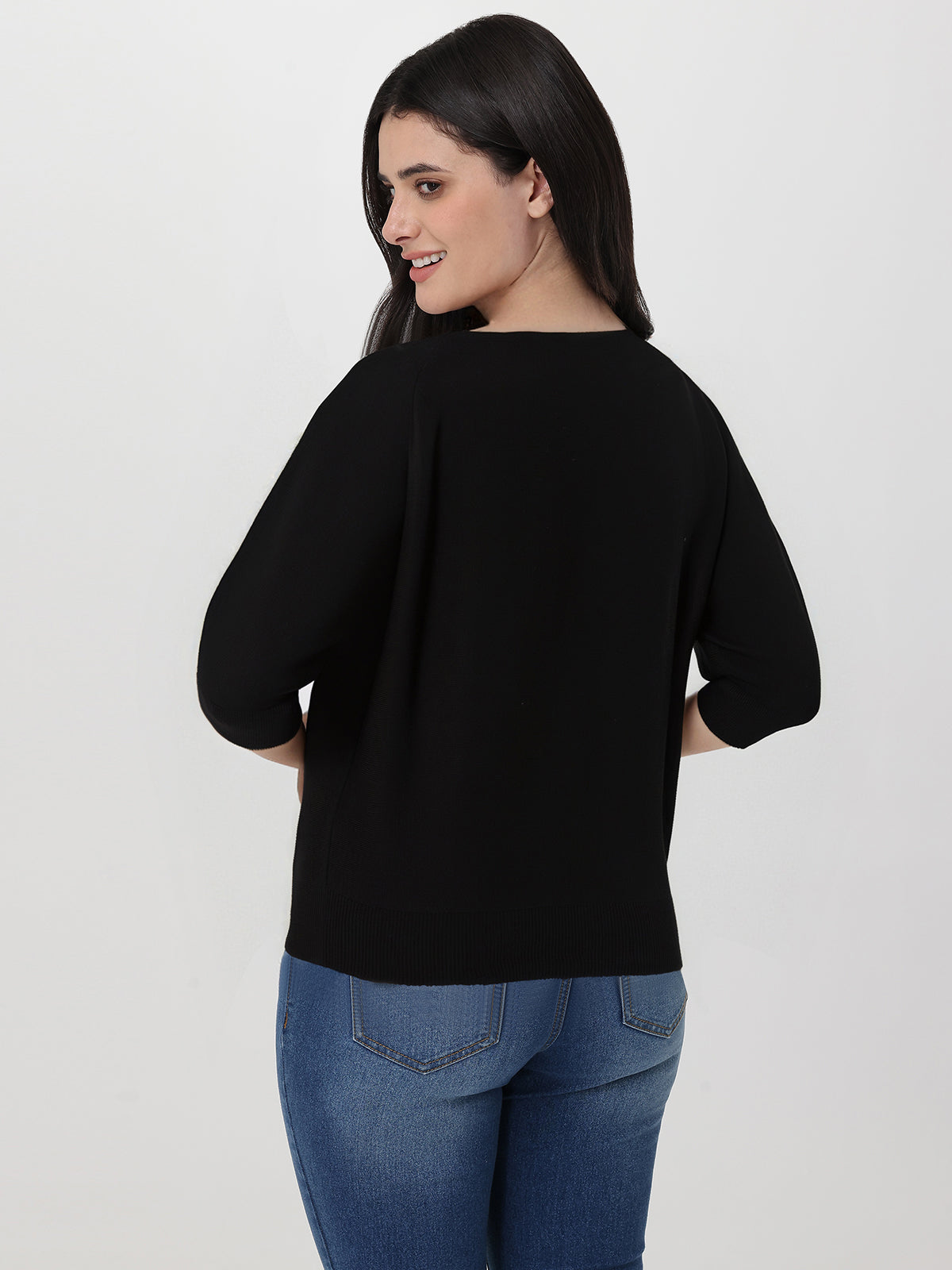 Woman wearing a black sweater and blue jeans on a white background