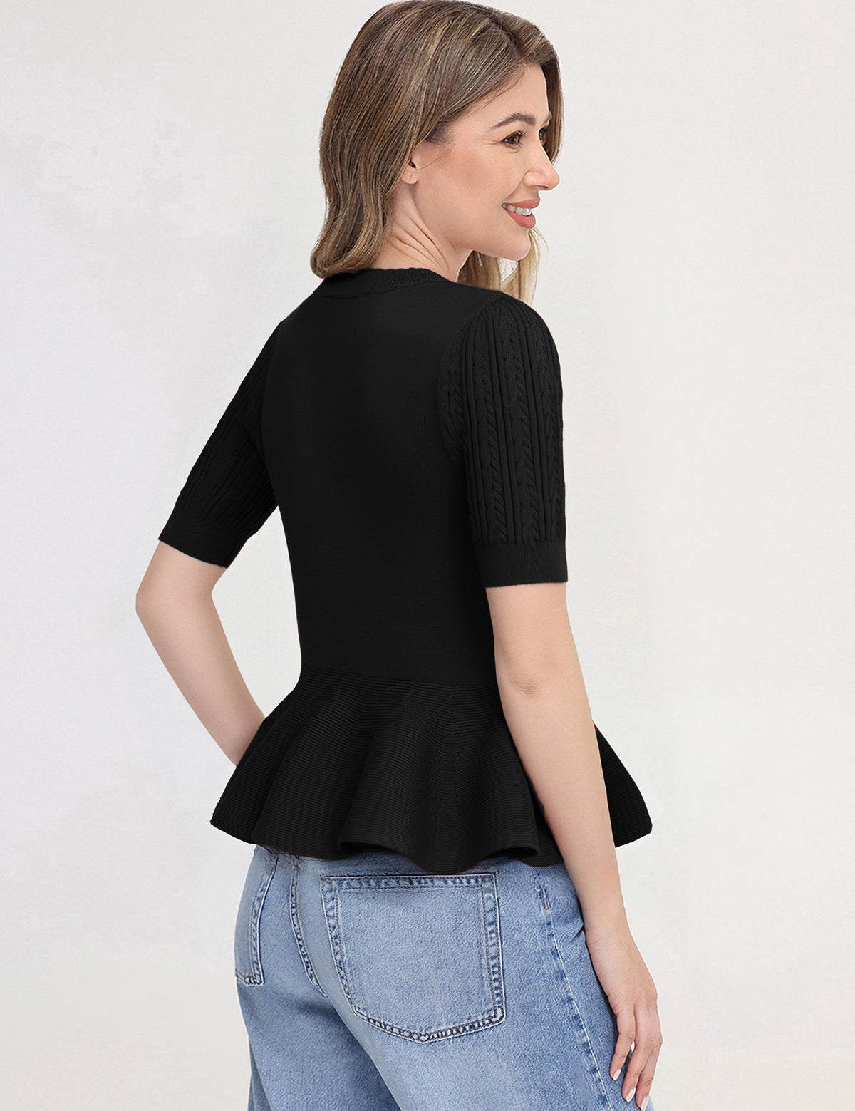 Woman wearing a black peplum top and blue jeans on a white background