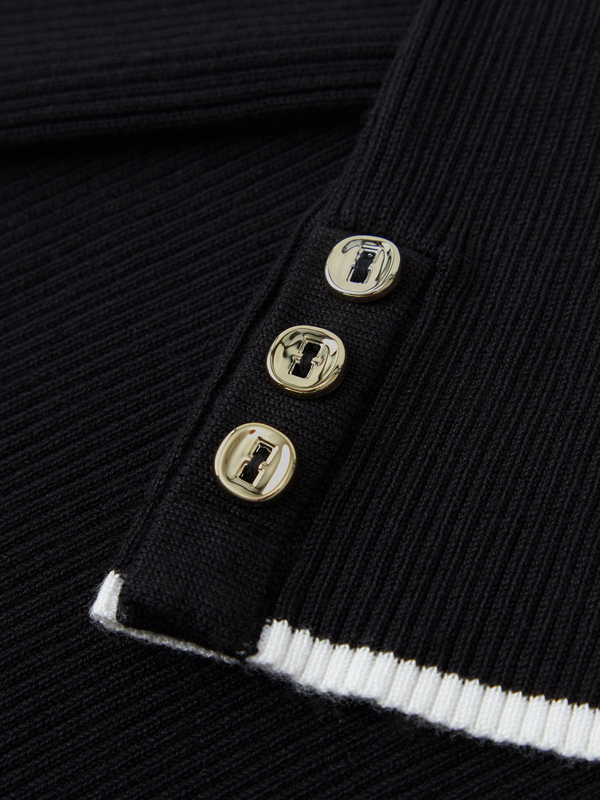 Close-up of a black ribbed sweater with gold buttons on a dark background