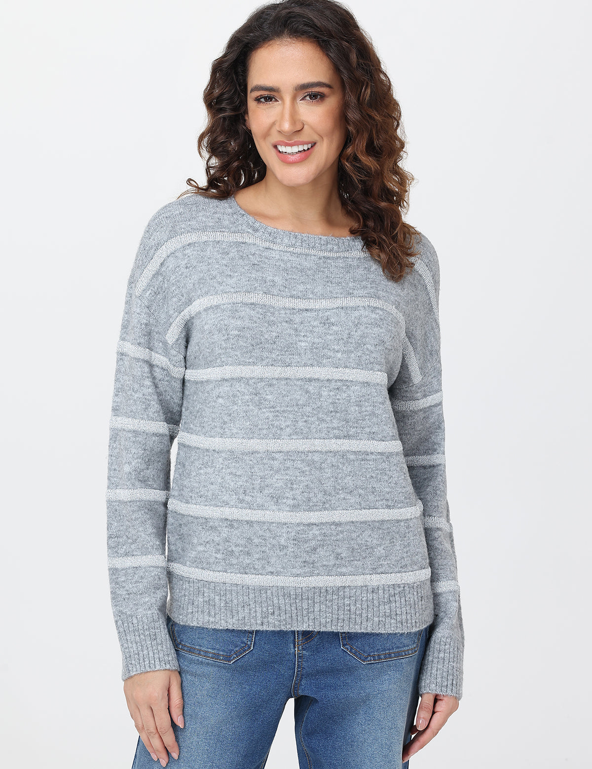 Woman wearing a gray striped sweater and blue jeans on a white background