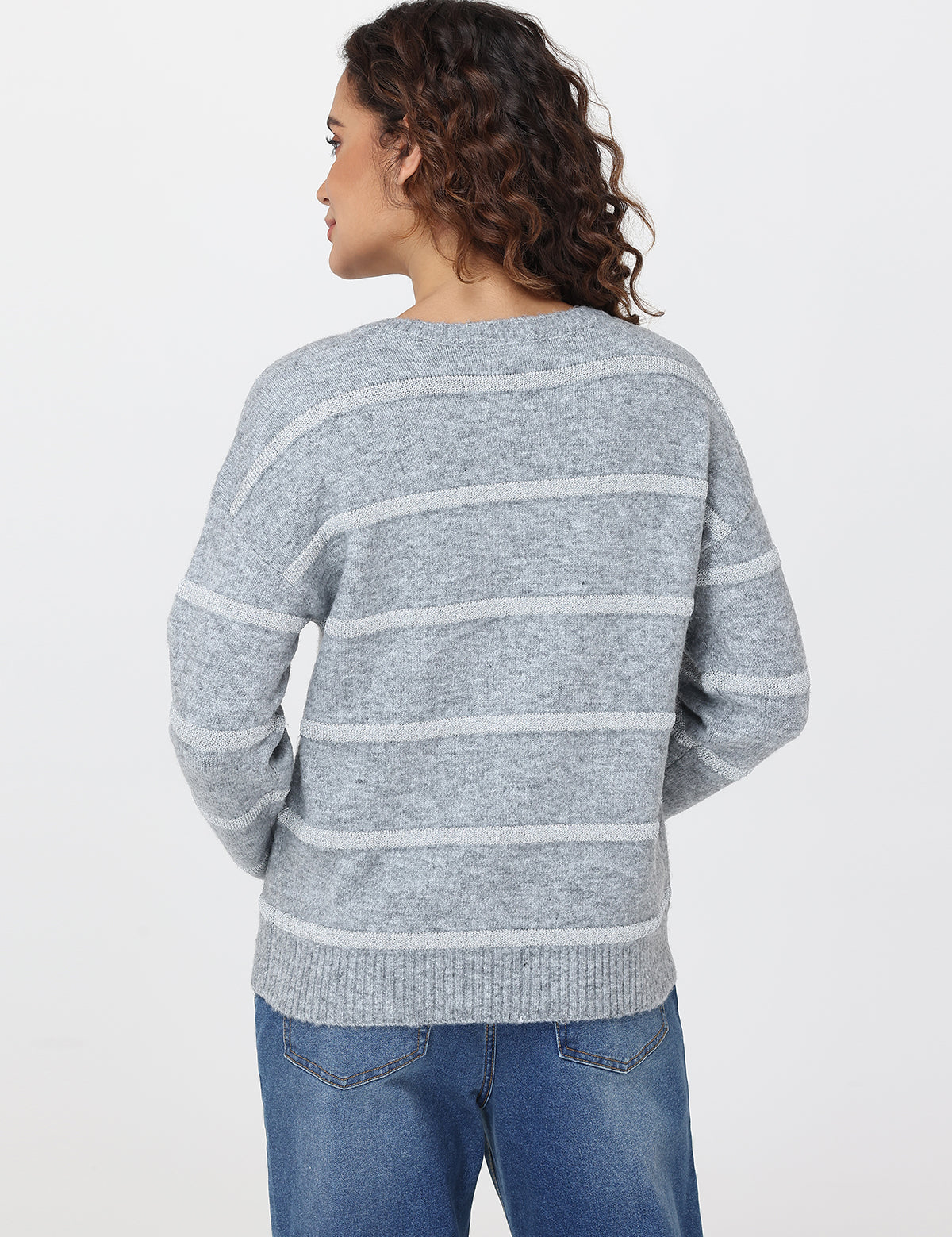 Person wearing a gray striped sweater and blue jeans on a white background