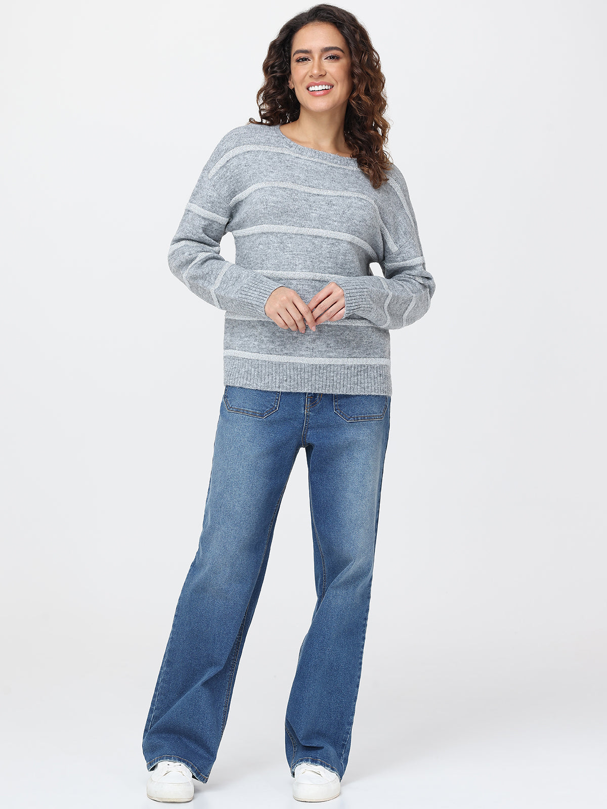 Woman wearing a gray striped sweater and blue jeans on a white background