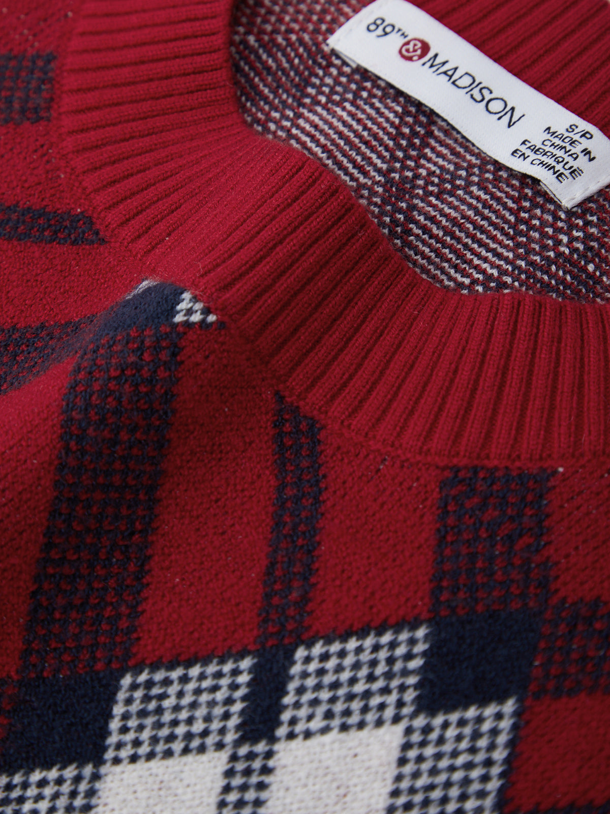 Close-up of a red plaid sweater with a brand label.