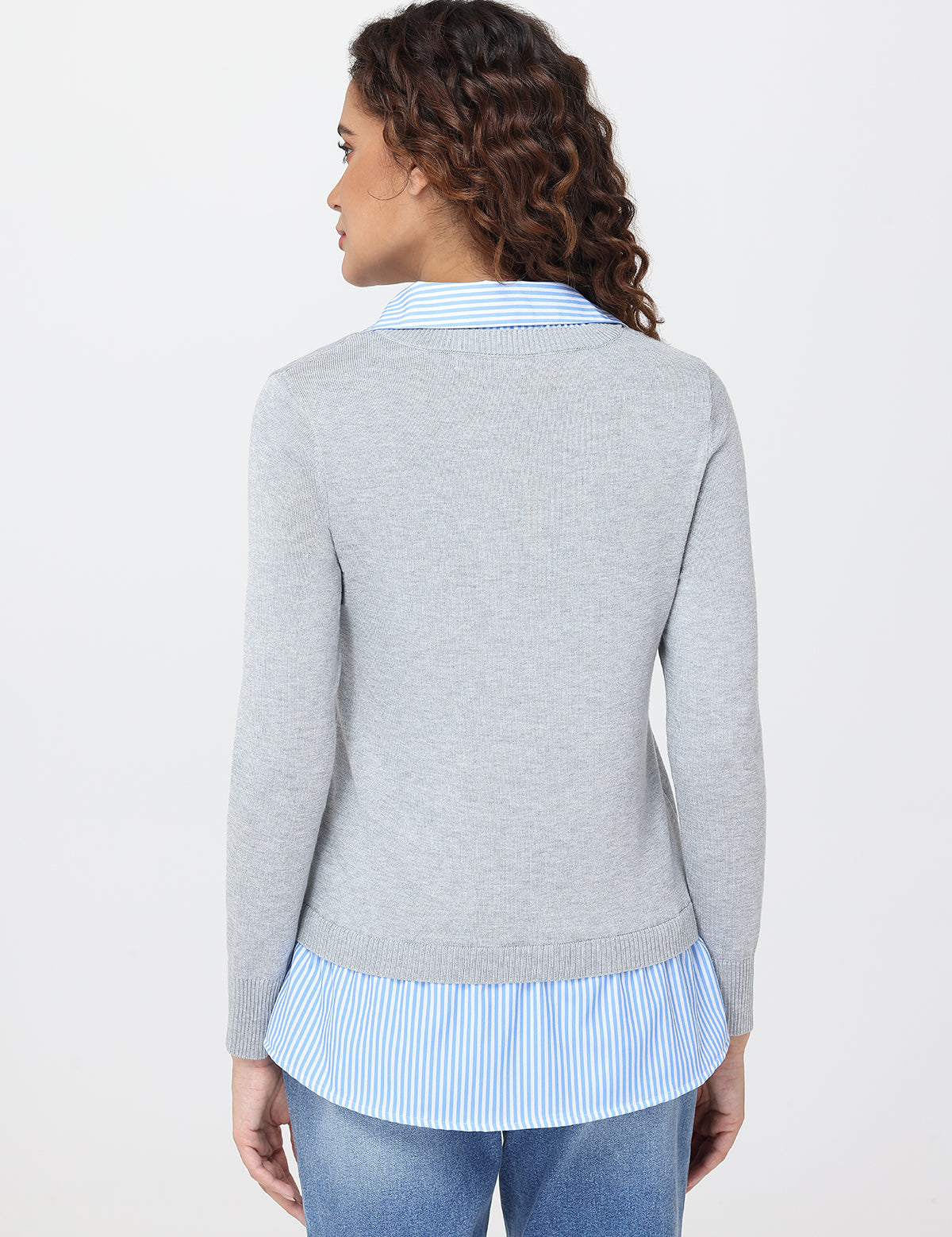 Woman wearing a gray sweater over a light blue striped shirt on a white background