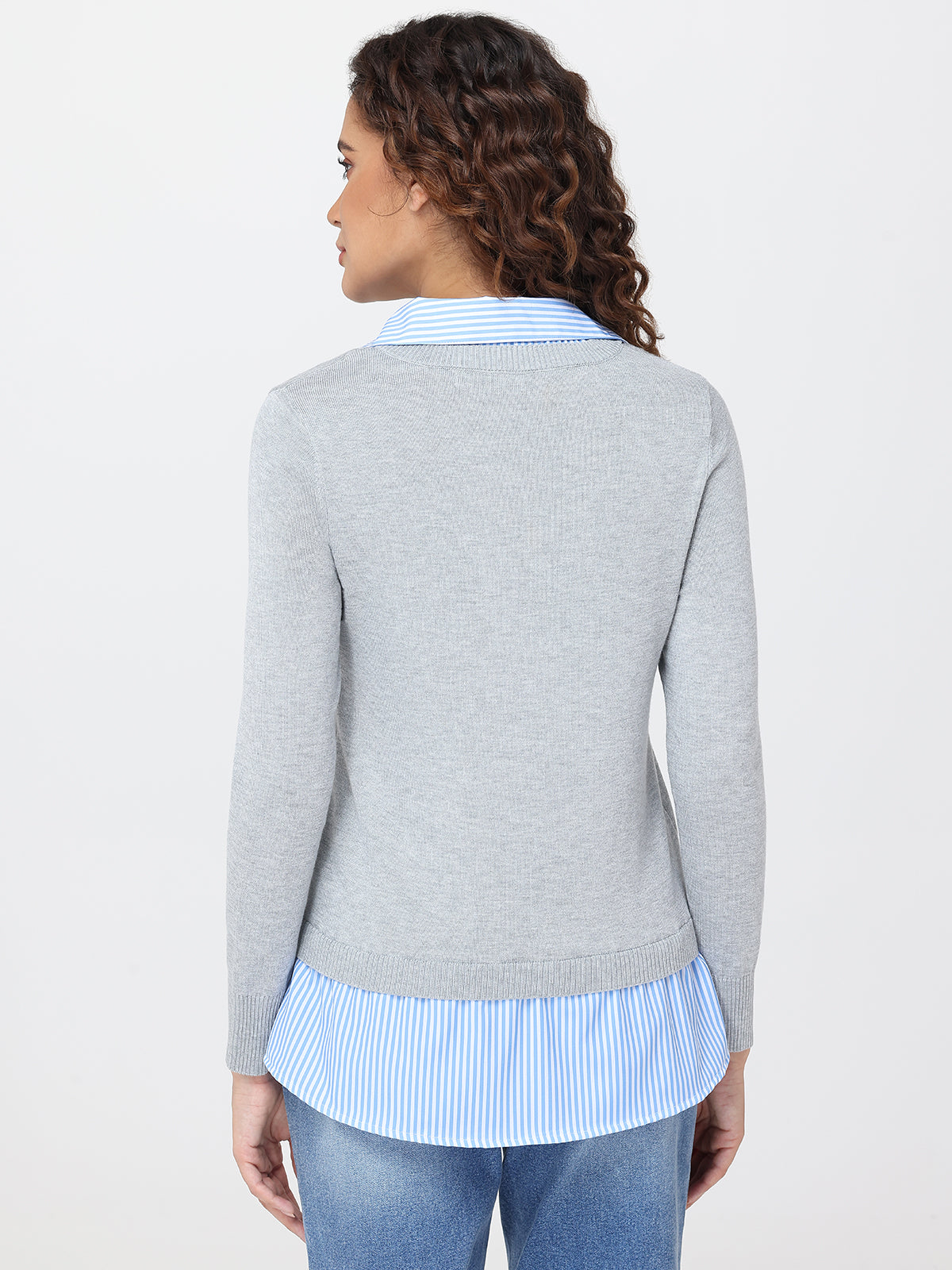 Woman wearing a gray sweater over a light blue striped shirt on a white background