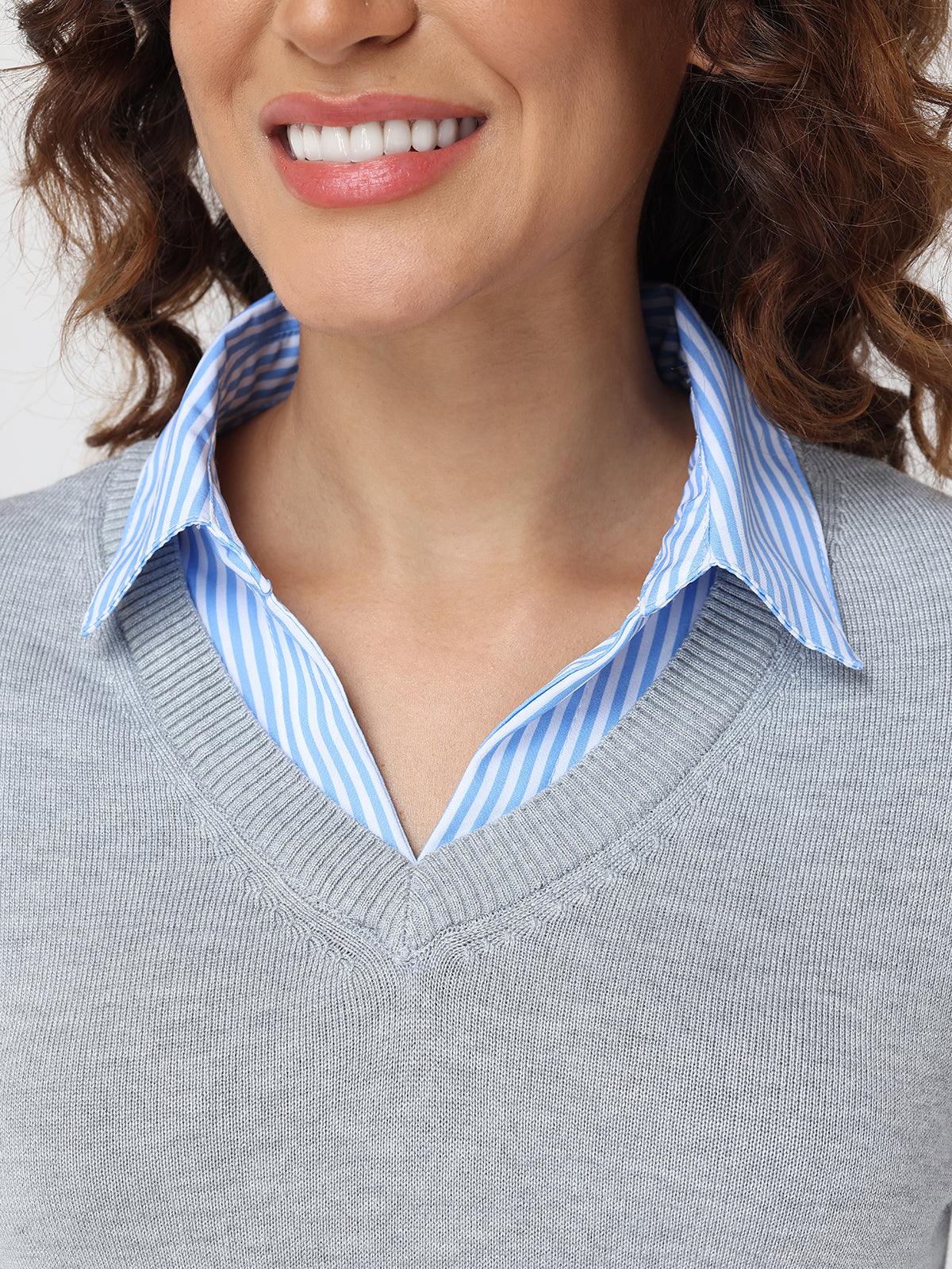 Person wearing a gray sweater with a blue and white striped shirt underneath