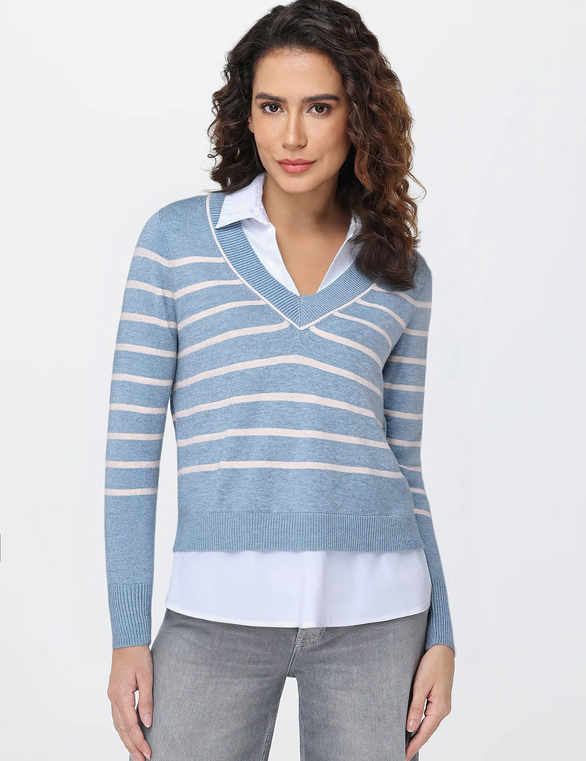 Woman wearing a blue and white striped sweater over a white shirt with gray pants on a light gray background