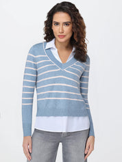 Woman wearing a blue and white striped sweater over a white shirt with gray pants on a light gray background
