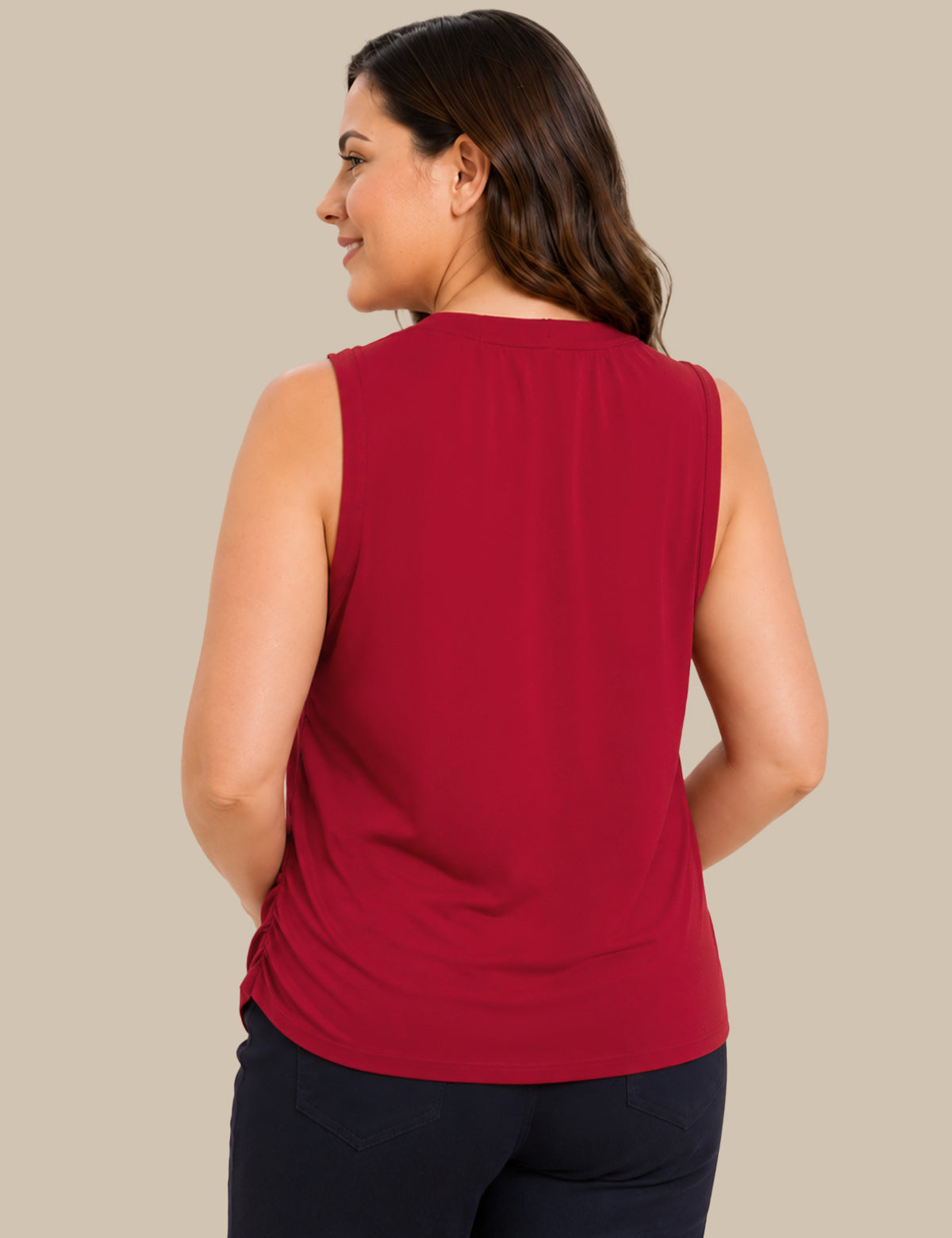A woman shown from the back wearing a sleeveless red top and dark pants, photographed against a plain beige studio background.