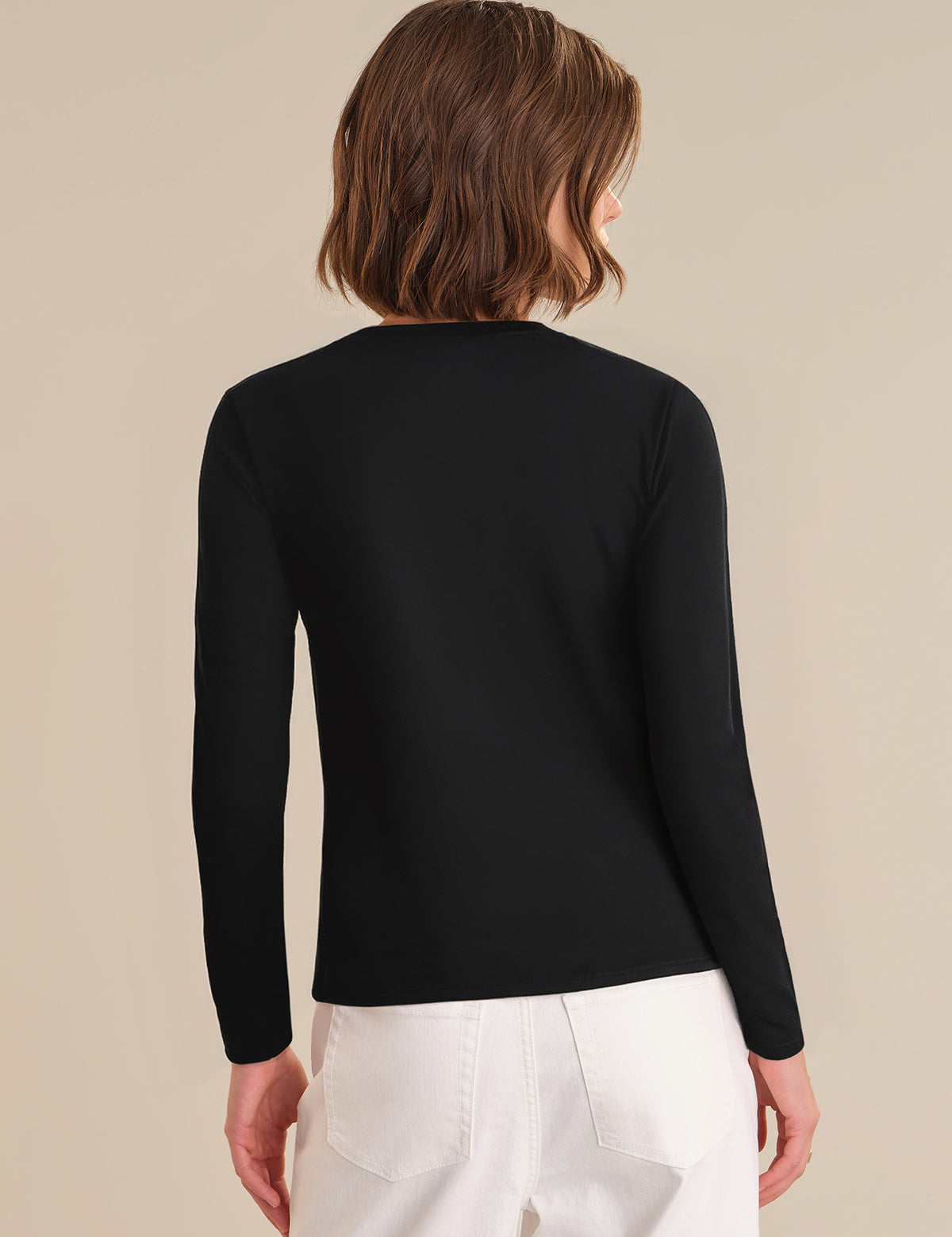Person wearing a black long-sleeve top and white pants on a beige background