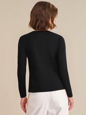 Person wearing a black long-sleeve top and white pants on a beige background