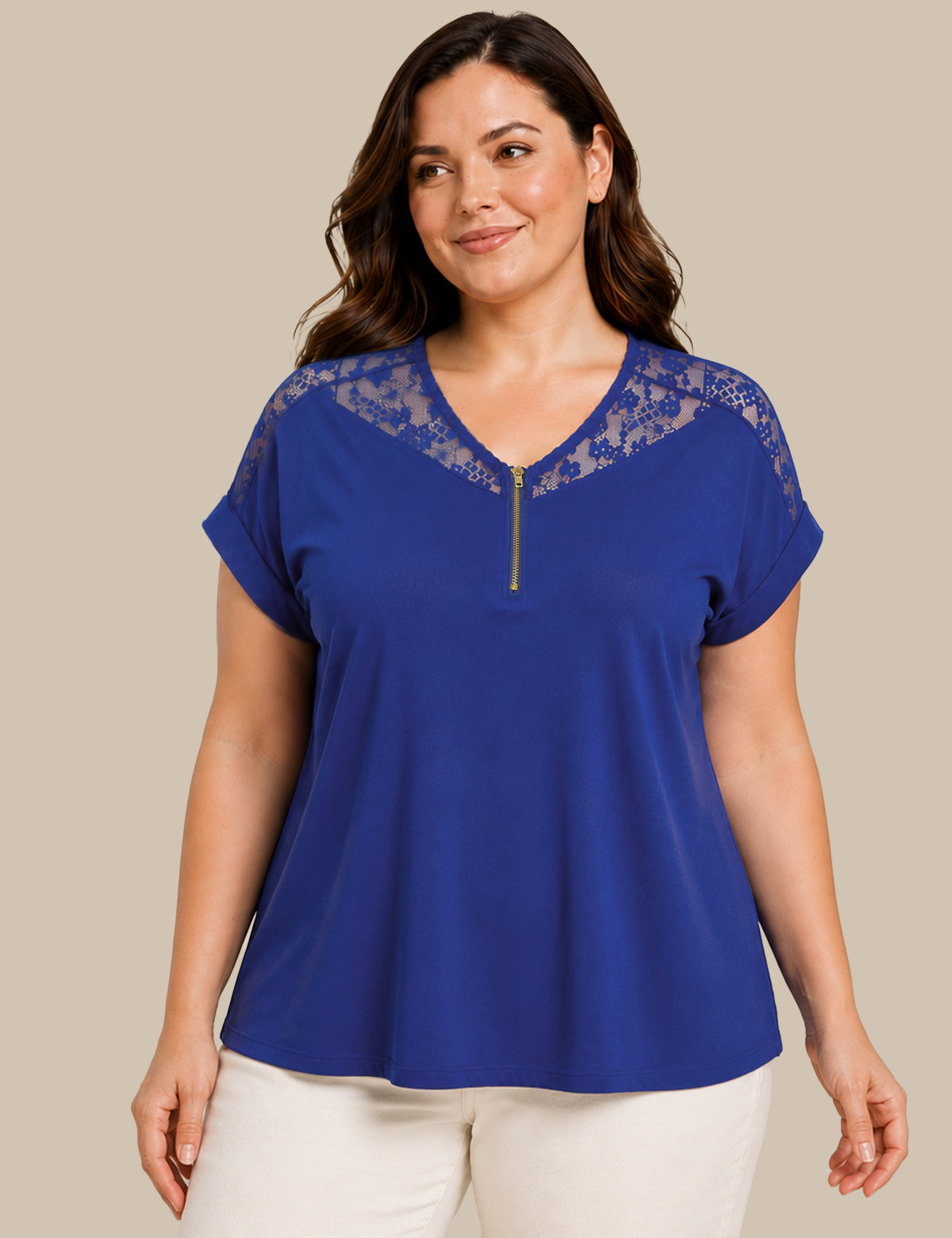 A woman wearing a royal blue short-sleeve top with a lace V-neckline and a small front zipper, paired with white pants, against a solid beige background.