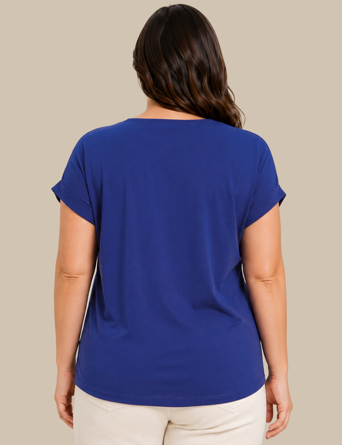 A woman viewed from the back wearing a royal blue short-sleeve top and cream pants, standing against a solid beige studio background.