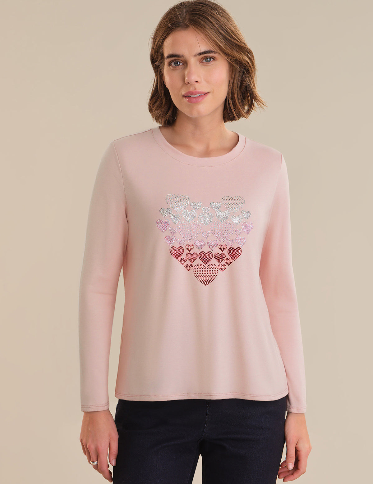 Woman wearing a pink long-sleeve top with a heart design on a beige background
