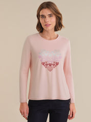 Woman wearing a pink long-sleeve top with a heart design on a beige background