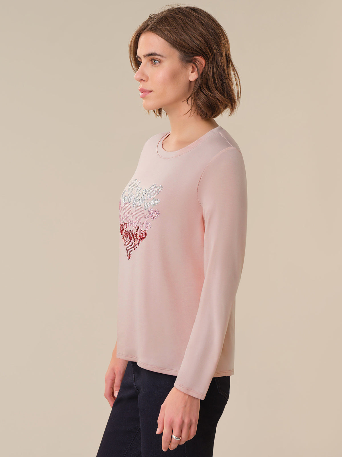 Woman wearing a light pink long-sleeve shirt with a graphic design on a beige background