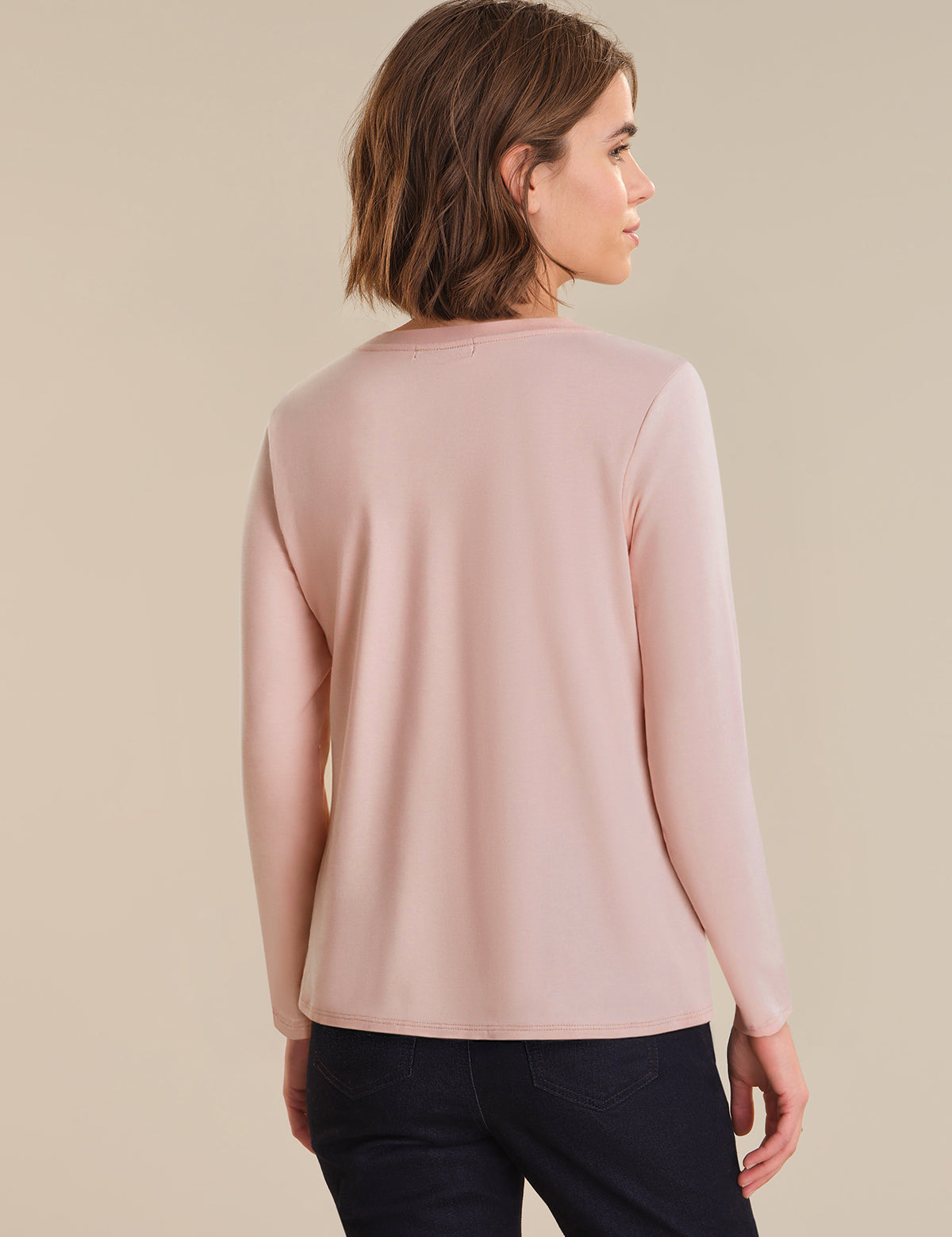 Woman wearing a light pink long-sleeve top against a beige background