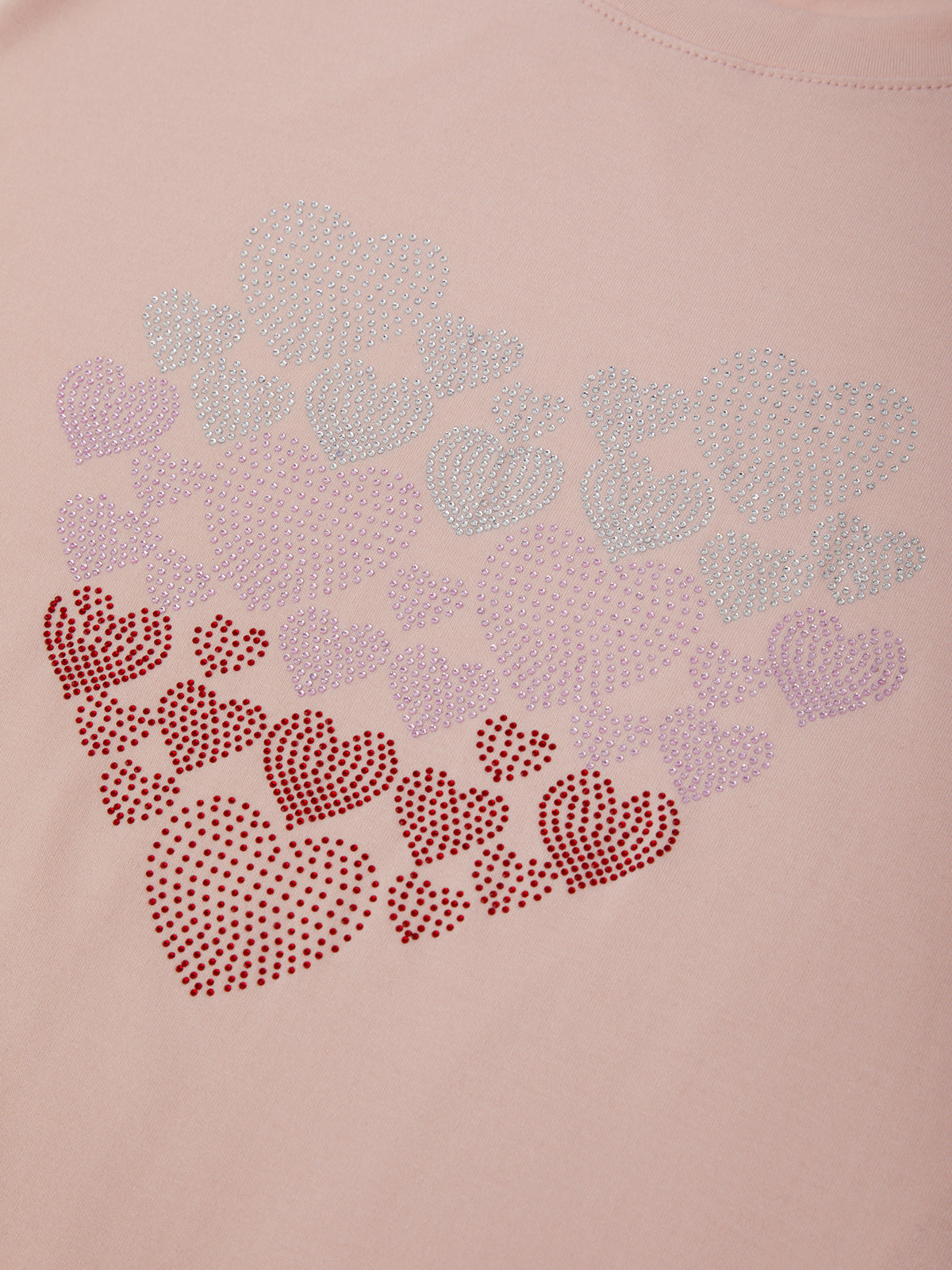 Pink sweatshirt with decorative heart patterns made of small stones on a light pink background