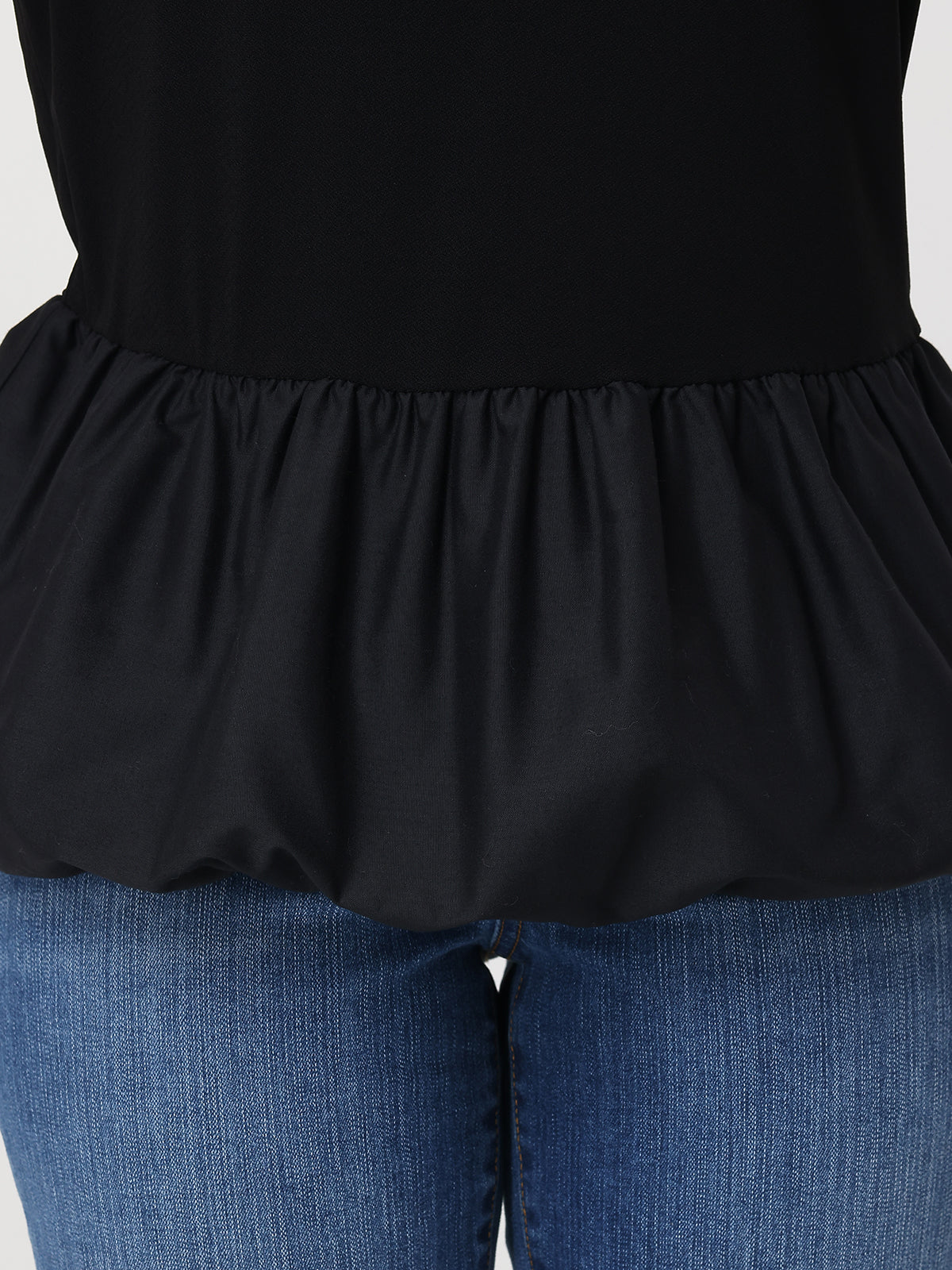 Black peplum top worn over blue jeans on a plain background