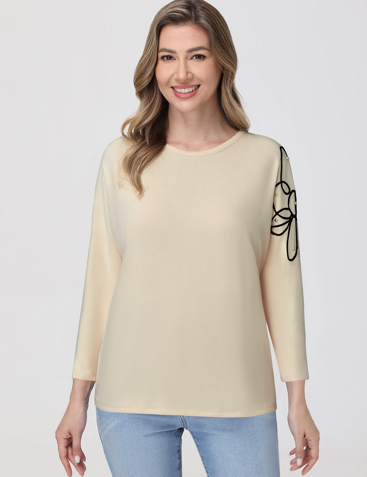Woman wearing a beige sweater with a black design on a plain background