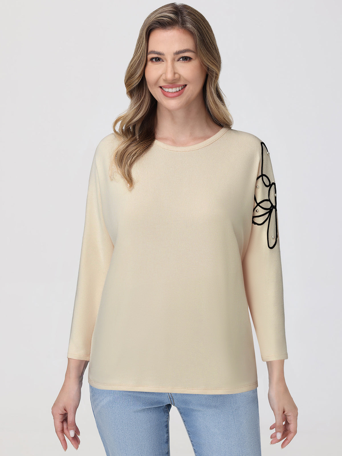 Woman wearing a beige sweater with a black design on a plain background