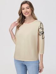 Woman wearing a beige top with a black butterfly design on a plain background