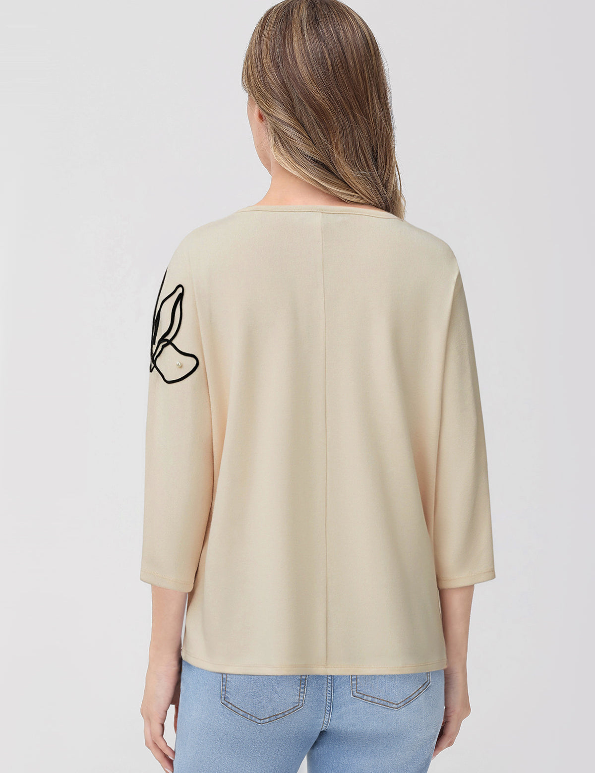Woman wearing a beige top with a black design on the sleeve against a white background