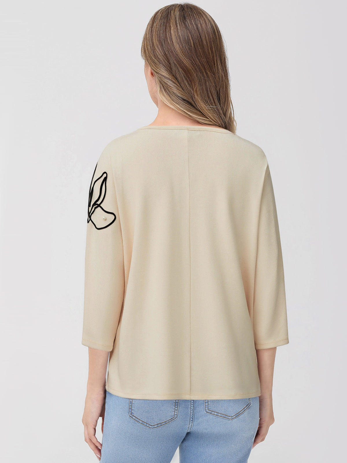 Woman wearing a beige top with a black design on the sleeve against a white background