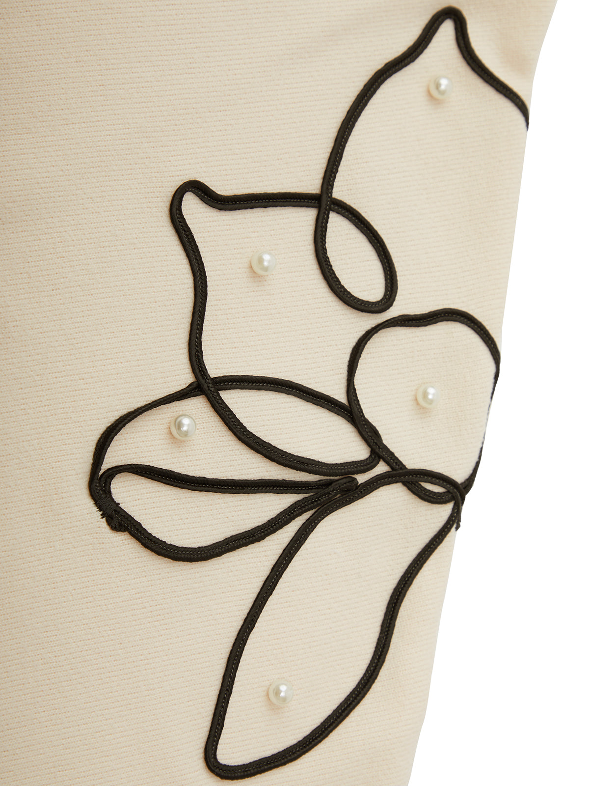Close-up of a beige garment with black embroidered design and pearl embellishments.
