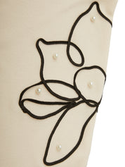 Close-up of a beige garment with black embroidered design and pearl embellishments.